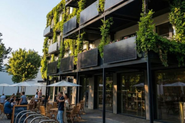 AuÃenansicht des Greenhouse Senden mit begrÃ¼nter Fassade, Solarmodulen und belebtem AuÃengastronomiebereich im Erdgeschoss.
